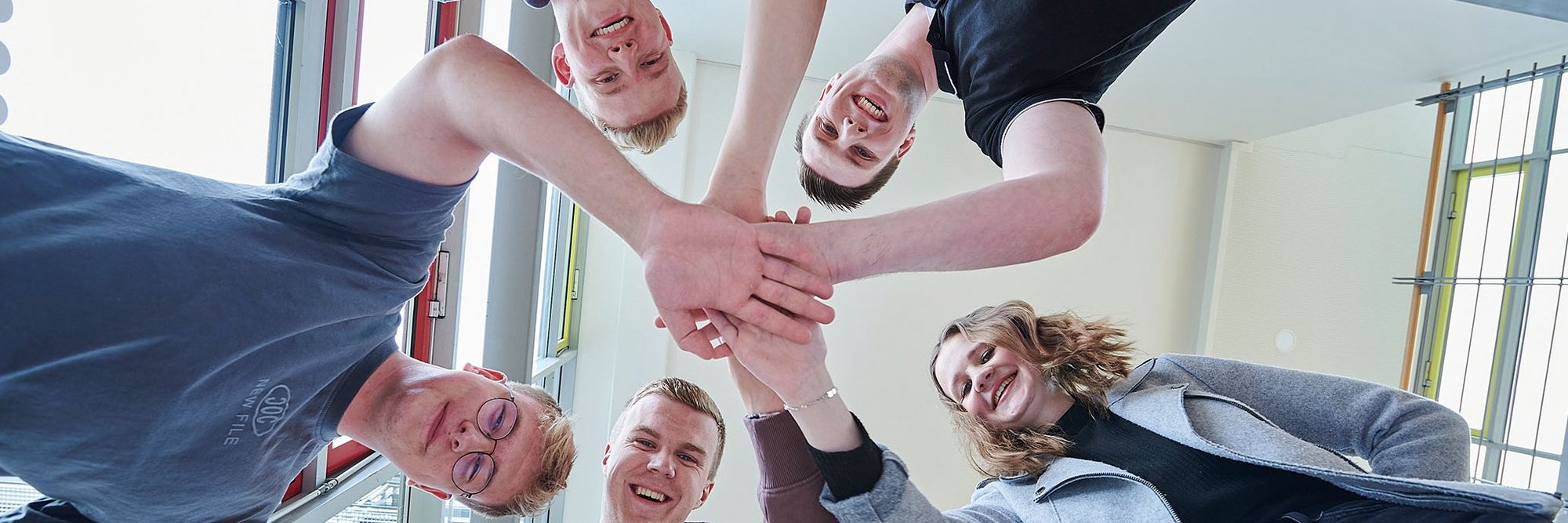 5 Personen stehen im Kreis zusammen und geben sich die Hände, von unten fotografiert