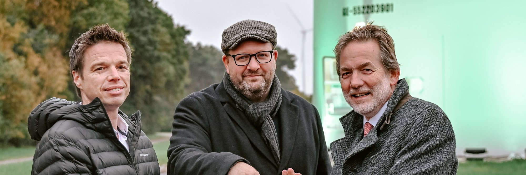 3 Männer vor der Windkraftanlage die einen roten Startbuzzer drücken